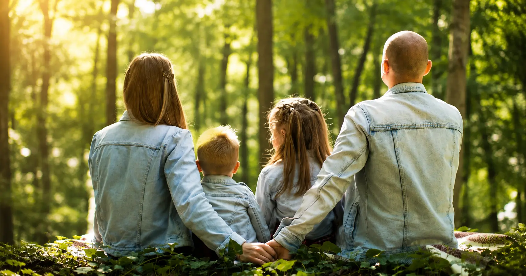 Family sitting together in a forest with parents holding hands behind their children.